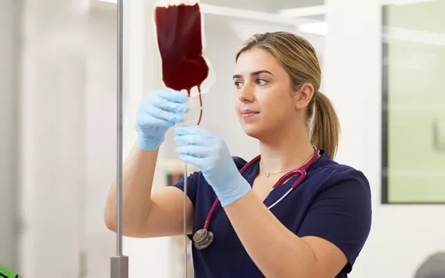 photograph of a nurse in blue scrubs wearing blue gloves putting a blood bag on a stand, to the left is the bandage design by Lisa Gorman