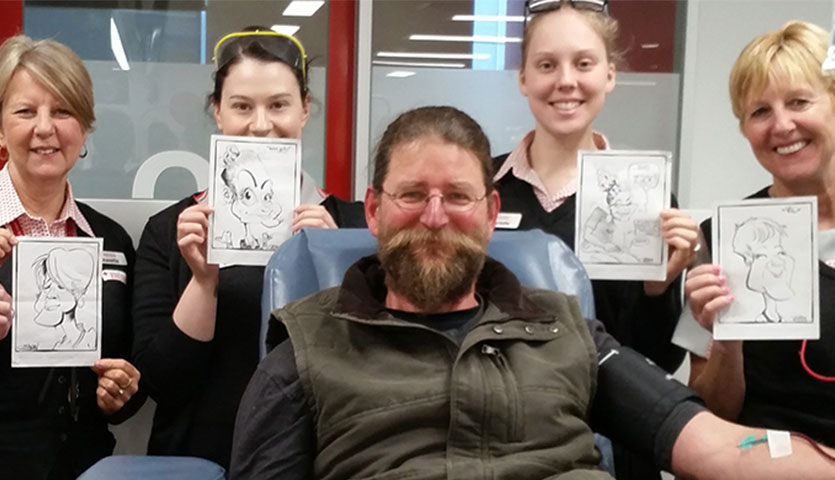 danny with donor centre staff holding up caricatures he has drawn