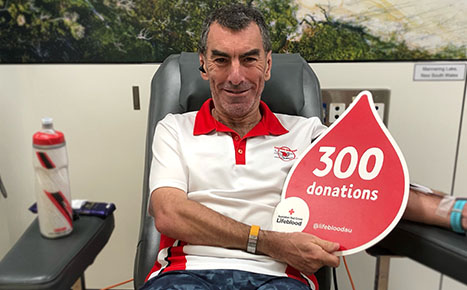 man smiling, donating blood and holding up a sign that says 300 donations