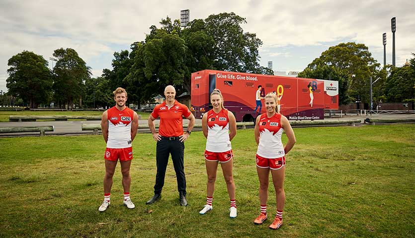 photo of sydney swans AFL player luke parker, CEO Tom Harley, player Montana Ham and Kiara Beesley standing on an oval with a Lifeblood mobile truck in the background