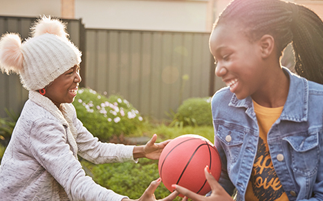 Two sisters sitting in their garden playing with a ball 