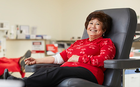 A female blood donor wearing read and smiling at the camera 