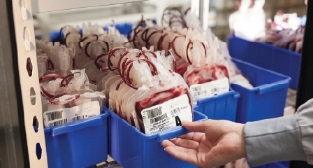 a hand picking up blood bags in a storage rack