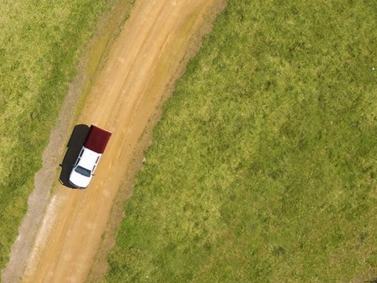 aerial photo of a field with a car driving on a dirt road throughit