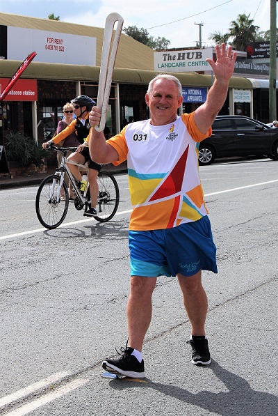 donor geoff is carrying the commonwealth games baton on a street and waving at the camera