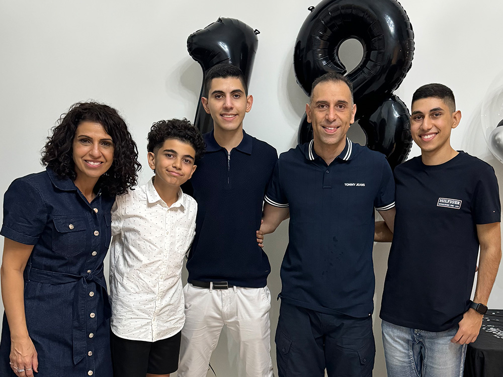 Family of five, including mum, dad and three sons smiling at the camera with an 18 balloon in the background