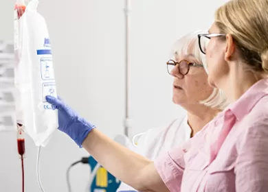 two nurses wearing pink gowns and blue gloves are examining an IV and discussing it