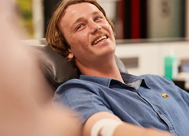 a man seated in a donor chair with a bandage around his right elbow and smiling