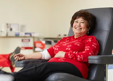 A female blood donor wearing read and smiling at the camera 