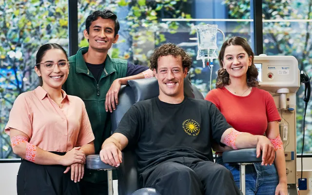 four people in a donor centre smiling at the camera, one is seated in a donor chair