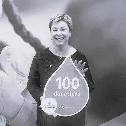 Black and white photo of a smiling woman holding a 100 milestone blood drop