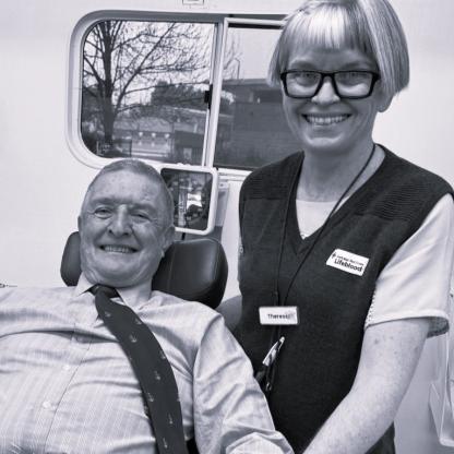 A man on a couch in a mobile donor unit with a nurse standing behind him. Both are smiling