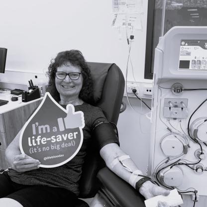 A woman smiling while donating and holding a I'm a lifesaver (it's no big deal) blood drop card