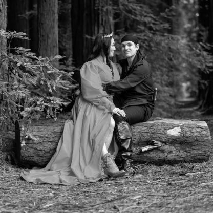 man and woman sitting on a fallen tree holding erach other, he is looking to camera