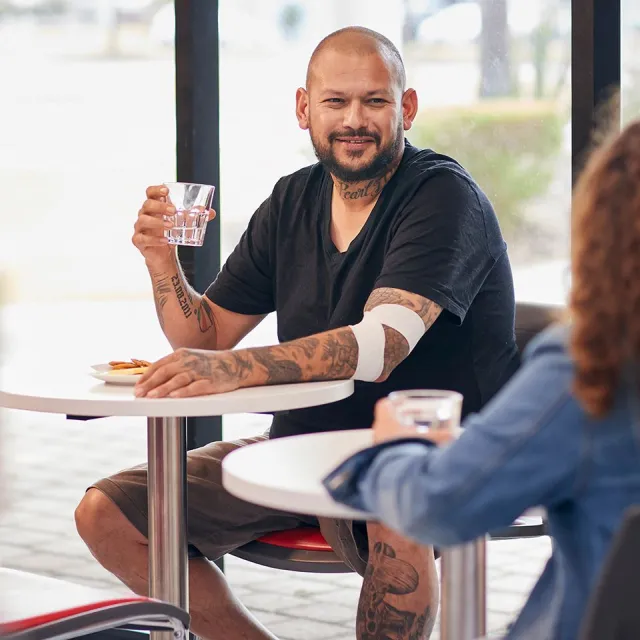 a man with tattoos and a bandage around an elbow seated at a table after a donation