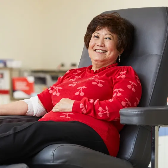 a woman in a donor chair smiling with a bandage around her elbow